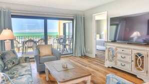 Un salón amplio con balcón con vistas a la playa, televisor y una zona de estar cómoda.