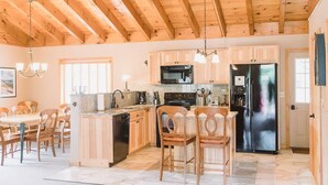A spacious kitchen with wooden cabinets, a black refrigerator, and a dining area with wooden chairs. - Mountain Home, Views, Near Whiteface, Lake Placid (Wilmington)