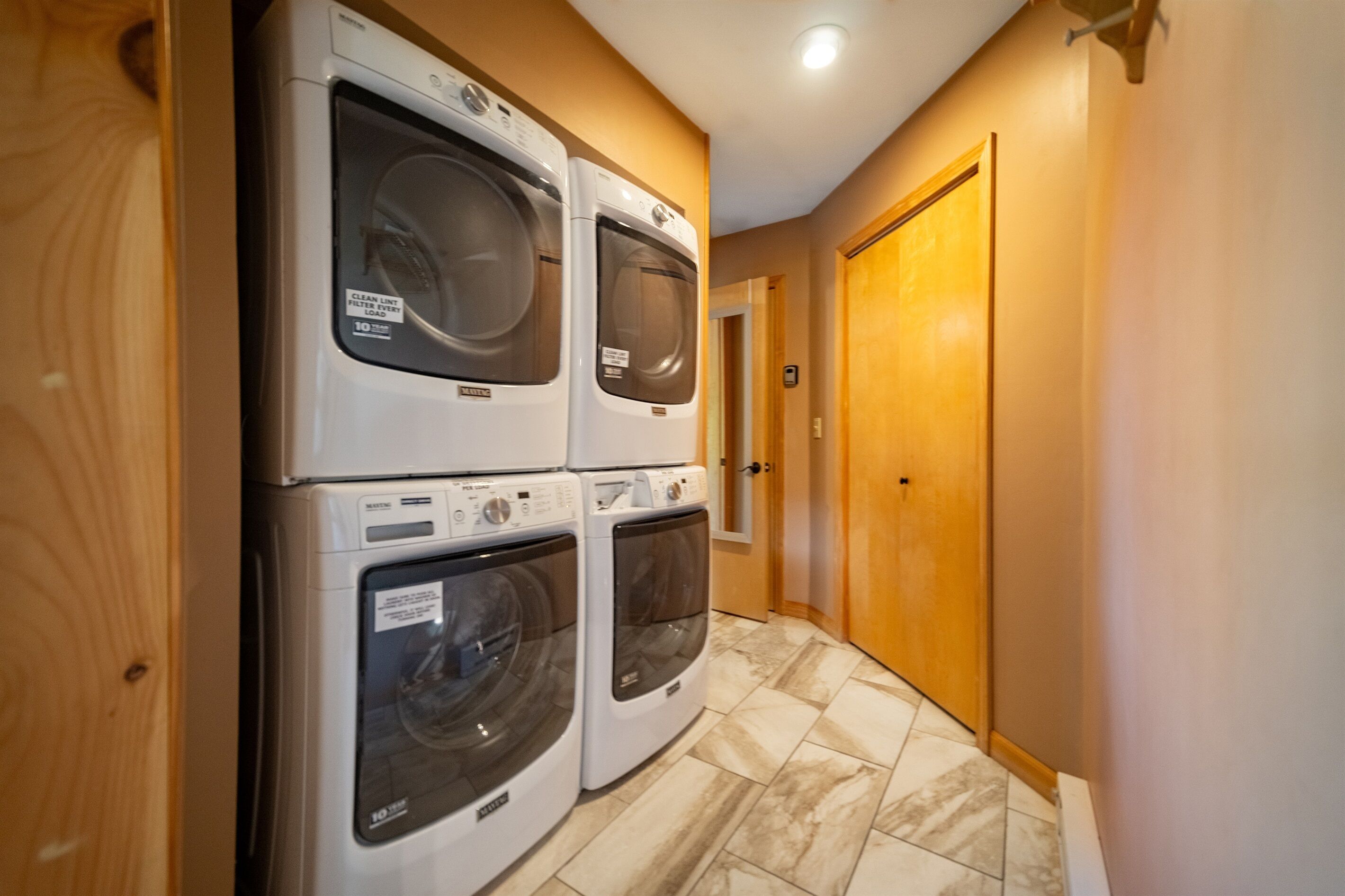 A laundry room with stacked washers and dryers, wooden walls, and a tiled floor.