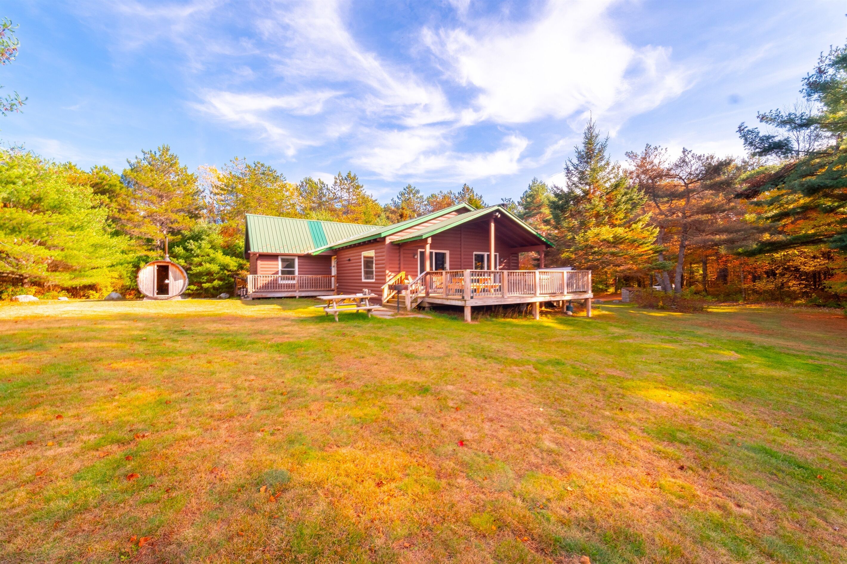 A cabin with a deck, surrounded by trees and a grassy yard.