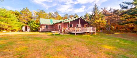 A cabin with a deck, surrounded by trees and a grassy yard.