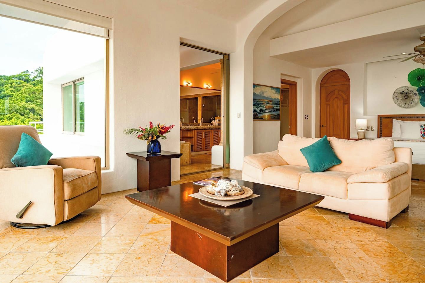 A spacious living area with a large window, a coffee table, a sofa, and a dining area in the background.