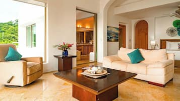 A spacious living area with a large window, a coffee table, a sofa, and a dining area in the background.