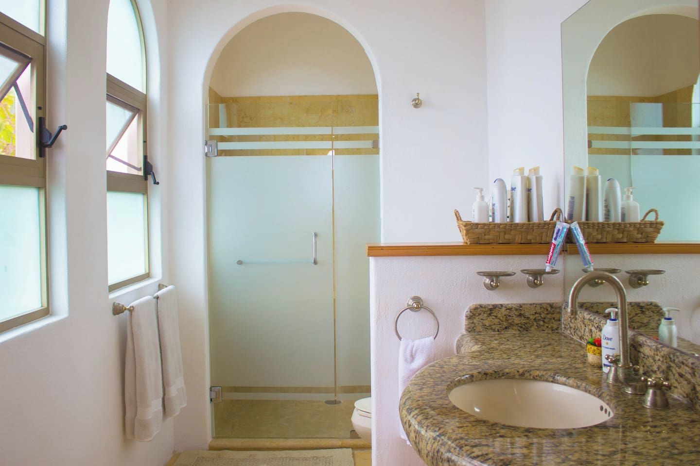 A bathroom with a granite sink, a mirror, a shower, and a towel rack.