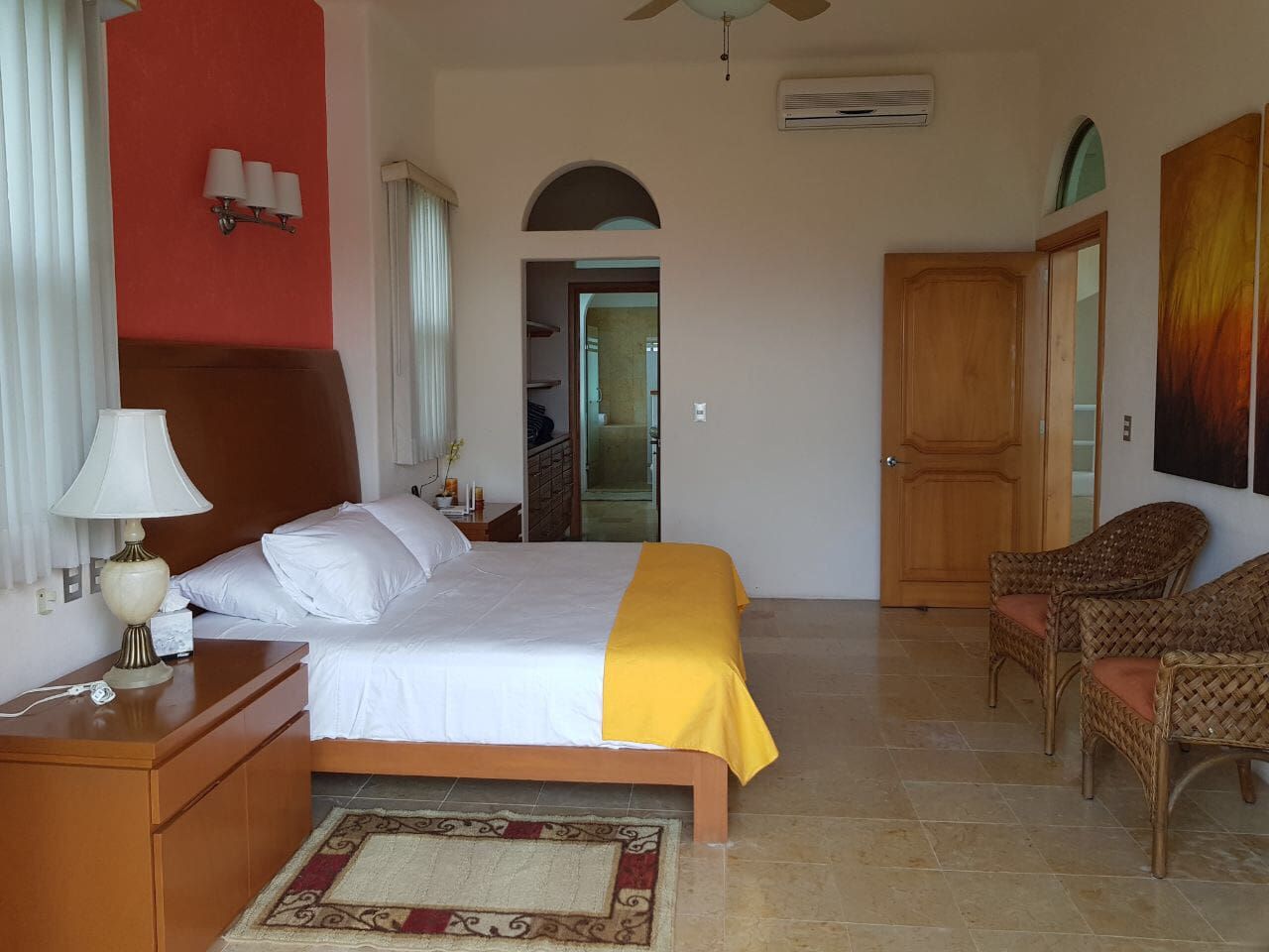 Quarto de hotel com cama, mesa de cabeceira, abajur, cadeira e porta.