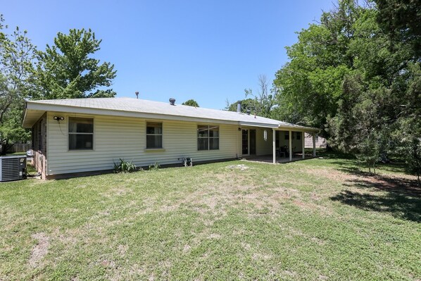 A single-story house with a covered porch, a small front yard, and a large tree to the right.