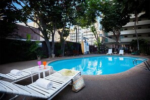 A swimming pool with lounge chairs and a table, surrounded by trees and a fence. - Action at your doorstep! Studio w/AC, WiFi, Kitchenette – Waikīkī Grand #618 (HONOLULU)