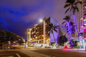 Een hotel met meerdere verdiepingen, balkons, een zebrapad en palmbomen.