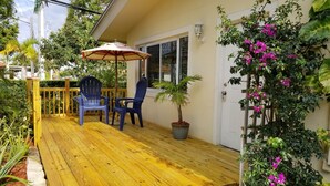 A wooden deck with two chairs and a striped umbrella, surrounded by lush greenery and flowering plants. - Newly Remodeled Home - Steps away from white sand beaches!!! (Lauderdale-By-The-Sea)