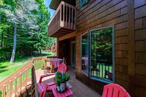Um deck de madeira com mesa e cadeiras, um vaso de planta e uma porta de vidro que dá para uma área externa coberta.