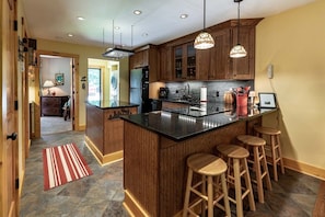 A kitchen with wooden cabinets, a central island with stools, and pendant lighting.