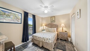 A bedroom with a bed, a nightstand, a ceiling fan, a window with curtains, and a painting on the wall.
