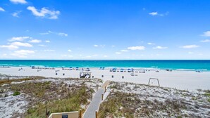 A beach with a wooden boardwalk leading to the shore, clear skies, and a calm sea.