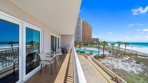 A balcony with a view of the beach, a pool, and a tall hotel building.