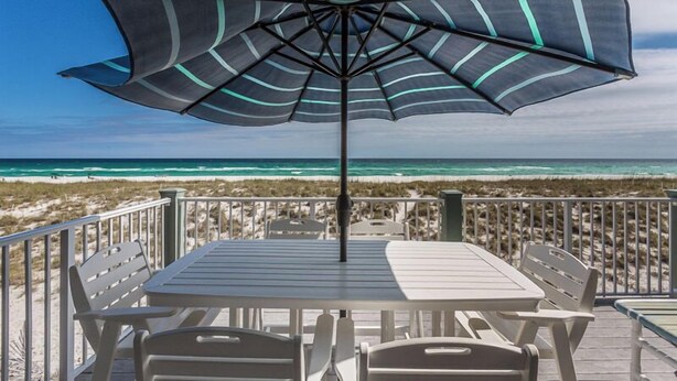 A beachside patio with a table and chairs, an umbrella, and a view of the ocean. - Drift Woods. Unforgettable Family Retreat – Gulf-Front Townhome on Navarre Beach (Navarre Beach)