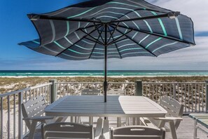 A beachside patio with a table and chairs, an umbrella, and a view of the ocean.