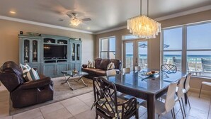 A spacious living area with a dining table, leather sofas, a TV cabinet, and large windows offering a view of the ocean. - Drift Woods. Unforgettable Family Retreat – Gulf-Front Townhome on Navarre Beach (Navarre Beach)