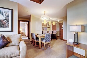 A spacious living area with a sofa, dining table, and chairs. There is a hallway leading to a kitchen area.