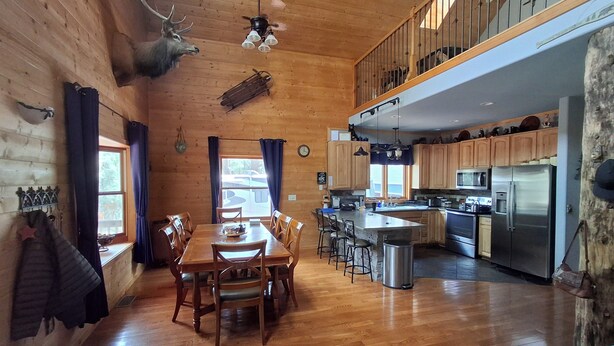 Interior de una cabaña de madera con comedor, cocina y un dormitorio en entrepiso.