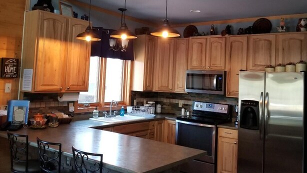 Una cocina con armarios de madera, un refrigerador de acero inoxidable, un microondas y una isla grande con taburetes de bar.