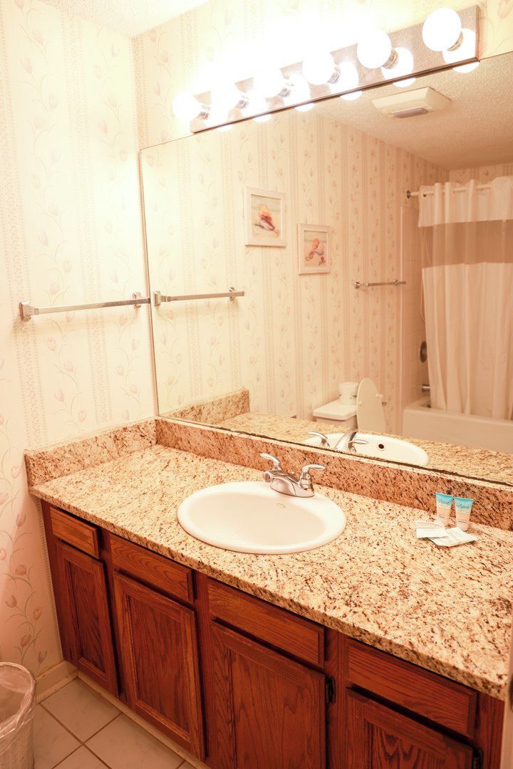 A bathroom with a granite countertop, a sink, a mirror, and a vanity with wooden cabinets.