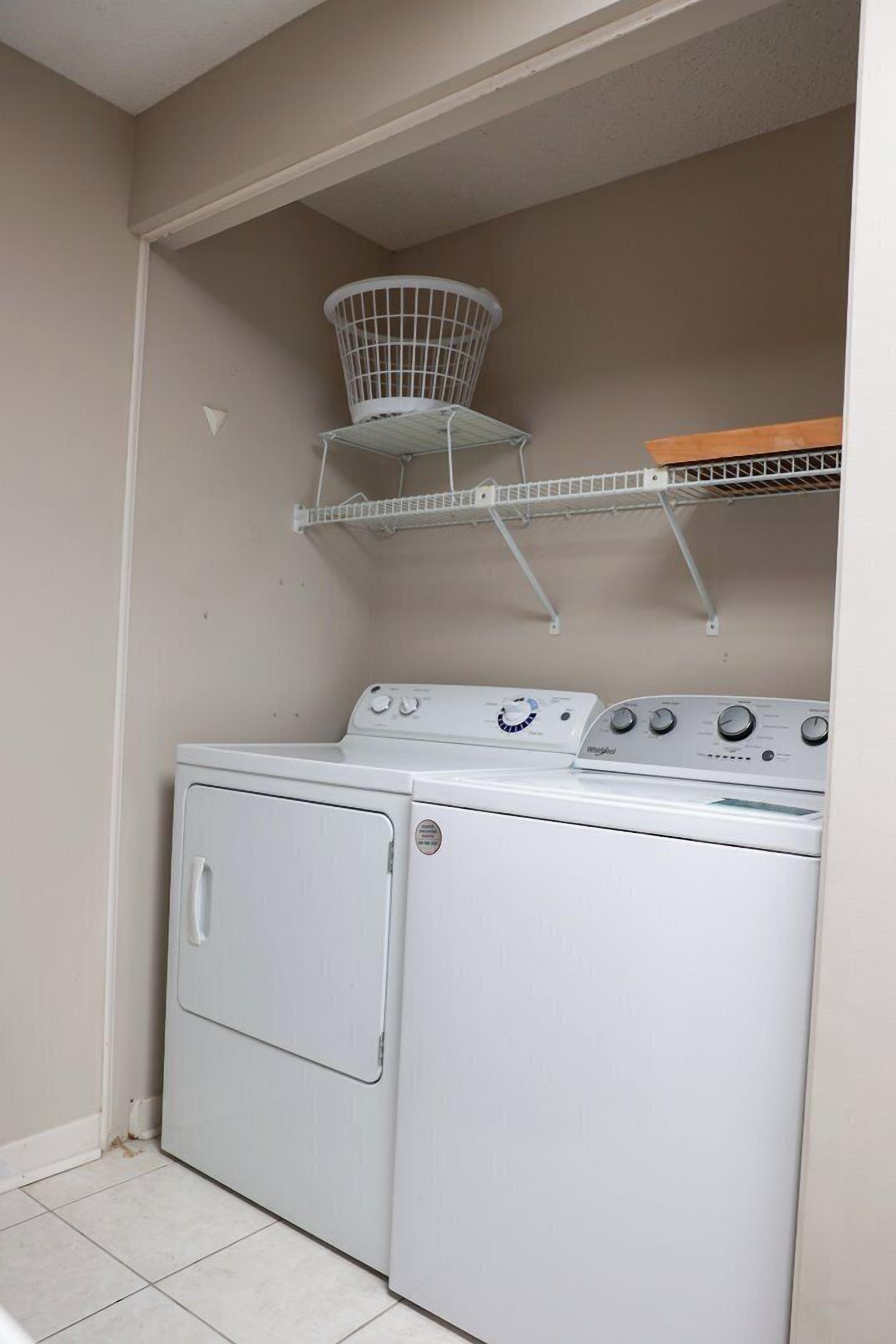 A laundry area with a front-loading washer and dryer, a metal drying rack, and a shelf above the dryer.