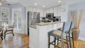 A modern kitchen with white cabinetry, stainless steel appliances, and a granite countertop. - 304 E Port by AvantStay | Rooftop Deck | Incredible Ocean & Beach Views! (Isle Of Palms)