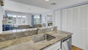 A modern kitchen with granite countertops, a stainless steel sink, and a built-in dishwasher. - 304 E Port by AvantStay | Rooftop Deck | Incredible Ocean & Beach Views! (Isle Of Palms)