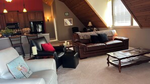 Ein gemütlicher Lofts-Wohnraum mit einer Küche, einem Ledersofa, einem weißen Sessel und einem Glastisch.