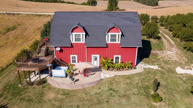 Ein rotes Bauernhaus mit schwarzem Dach, einer Terrasse und einem Whirlpool.
