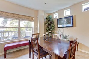 A dining room with a wooden table, six chairs, a bench, and a TV mounted on the wall.
