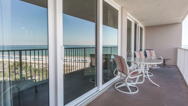 Een balkon met een glazen deur, een tafel met stoelen en uitzicht op het strand.