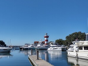 A marina with several yachts docked, a prominent lighthouse, and a clear blue sky.