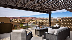 An outdoor patio with wicker furniture, a fire pit, and a view of a desert landscape. - Stunning Red Rock Views - 4BR Poolside Fire Pit (St. George)