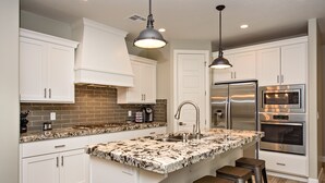 A kitchen with white cabinets, a granite island, stainless steel appliances, and pendant lighting. - Stunning Red Rock Views - 4BR Poolside Fire Pit (St. George)