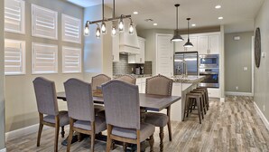 A dining area with a wooden table and chairs, a kitchen with white cabinets and stainless steel appliances, and a patterned floor. - Stunning Red Rock Views - 4BR Poolside Fire Pit (St. George)