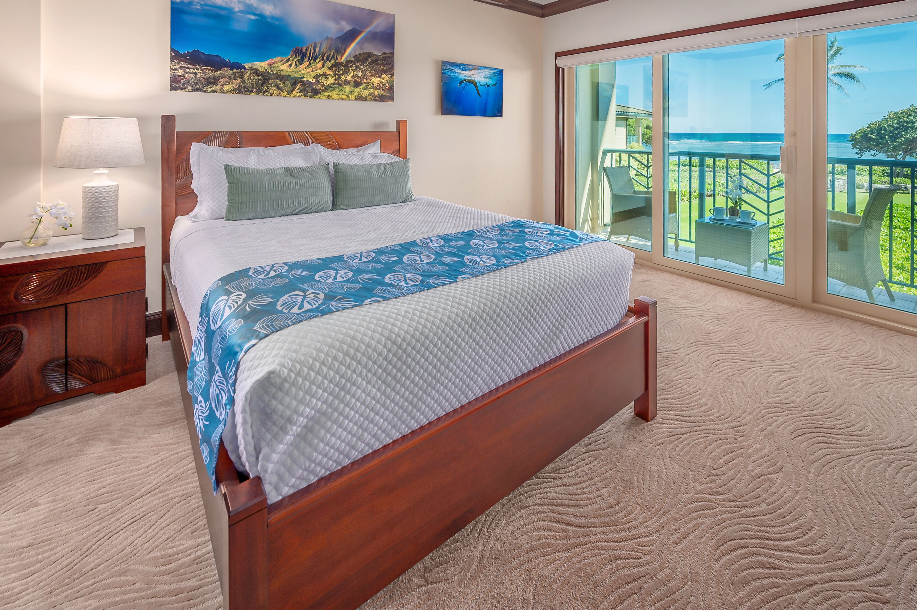 A bedroom with a large bed, a nightstand, a lamp, and a view of the ocean through a sliding glass door.