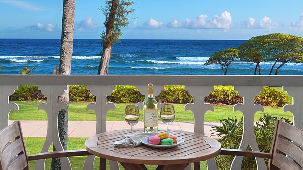 Un tavolo con due bicchieri da vino, una bottiglia e dei macarons su un balcone con vista sull'oceano.
