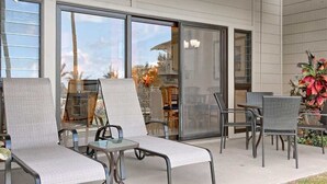A covered outdoor seating area with lounge chairs and a table, large sliding glass doors, and a view of the outdoors. - Peaceful Paradise! Spacious Condo, Full Kitchen, Wifi, Flat Screens-Kaha Lani 108 (LIHUE)