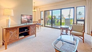 A spacious living room with a large TV, a glass coffee table, and a ceiling fan. - Peaceful Paradise! Spacious Condo, Full Kitchen, Wifi, Flat Screens-Kaha Lani 108 (LIHUE)