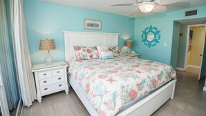 A bedroom with a bed, nightstands, a ceiling fan, and a decorative mirror. - C106 Low Floor, Stunning sunset, Pool View, covered parking space (Panama City Beach)