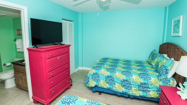 A bedroom with a bed, a dresser, a television, and a bathroom visible through an open door.