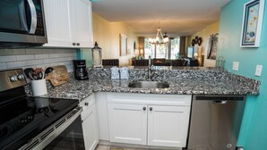 A kitchen with white cabinets, a granite countertop, a stainless steel sink, a coffee maker, and a dishwasher. - C106 Low Floor, Stunning sunset, Pool View, covered parking space (Panama City Beach)