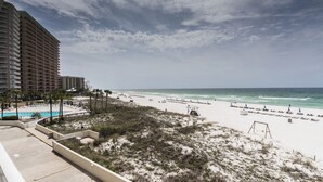 A beach view with a pool, beach chairs, and umbrellas.