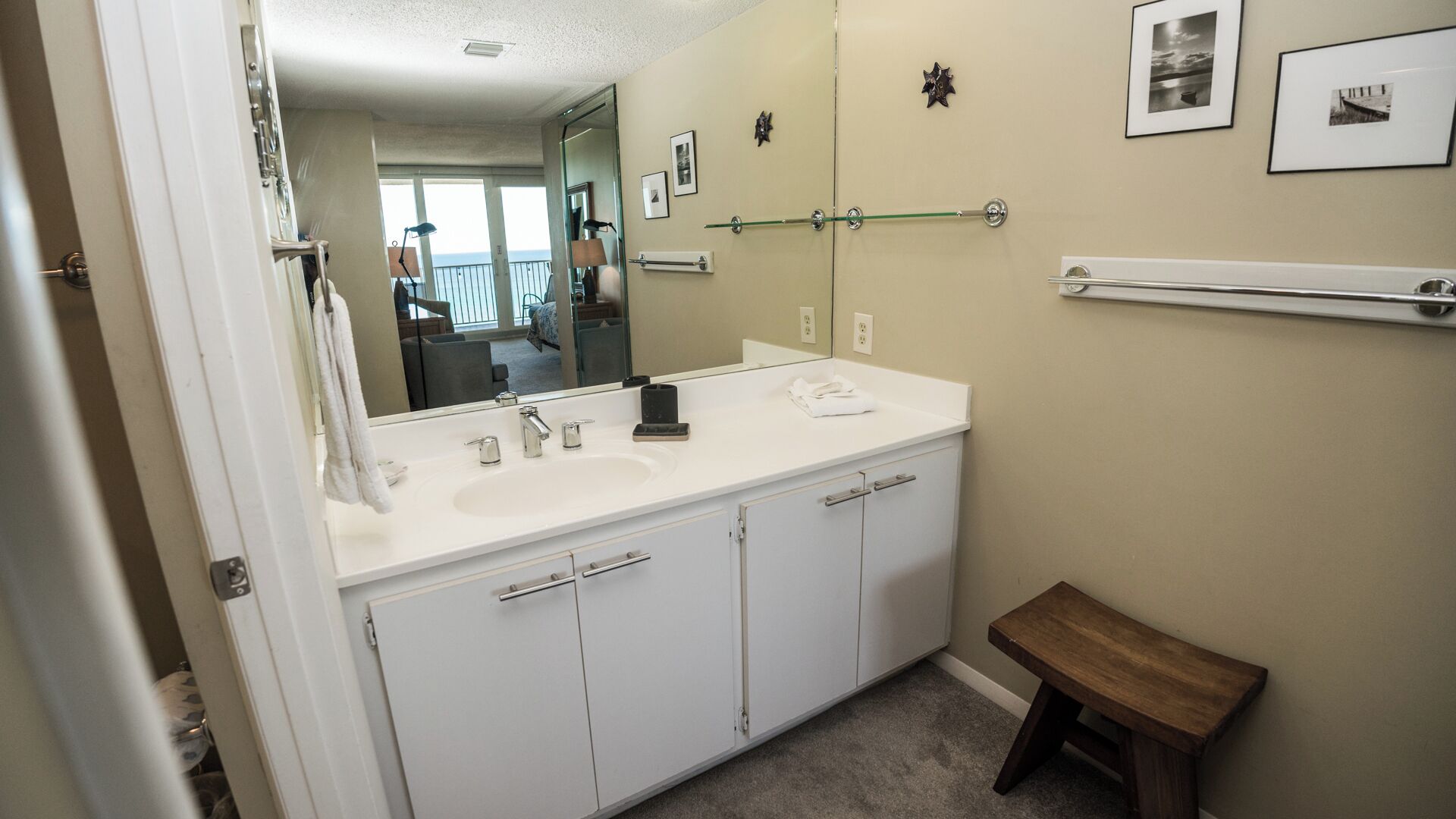 A bathroom with a white vanity, a large mirror, and a wooden bench.