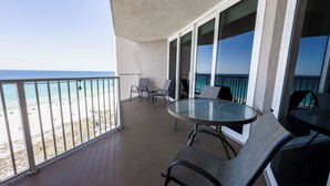 Balcón con mesa y sillas de vidrio, con vista a una playa.