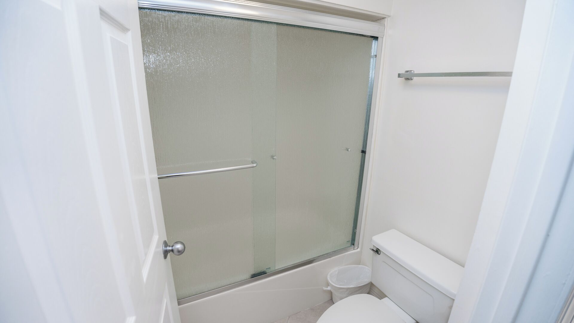 Une salle de bain avec une douche à parois de verre, des toilettes et une petite poubelle.