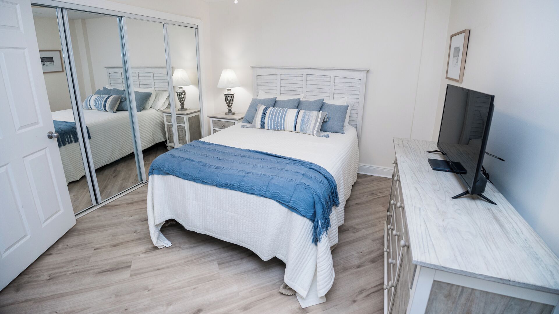 A bedroom with a bed, a TV, a wardrobe, and a mirror.