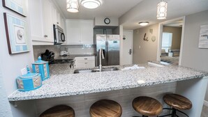 A modern kitchen with white cabinets, granite countertops, stainless steel appliances, and a bar area with stools. - D504 Gulf Front Views, 3 pools, Tennis (Panama City Beach)