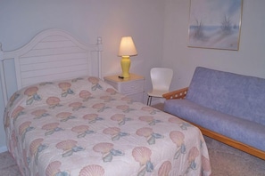 A bedroom with a bed, a nightstand with a lamp, a chair, and a sofa.
